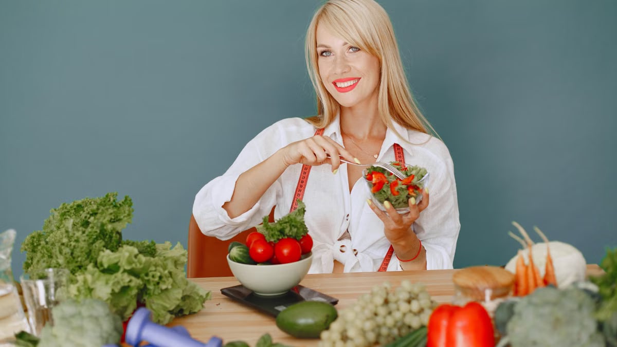 Blonde woman enjoying a fresh salad surrounded by vegetables, promoting healthy eating.