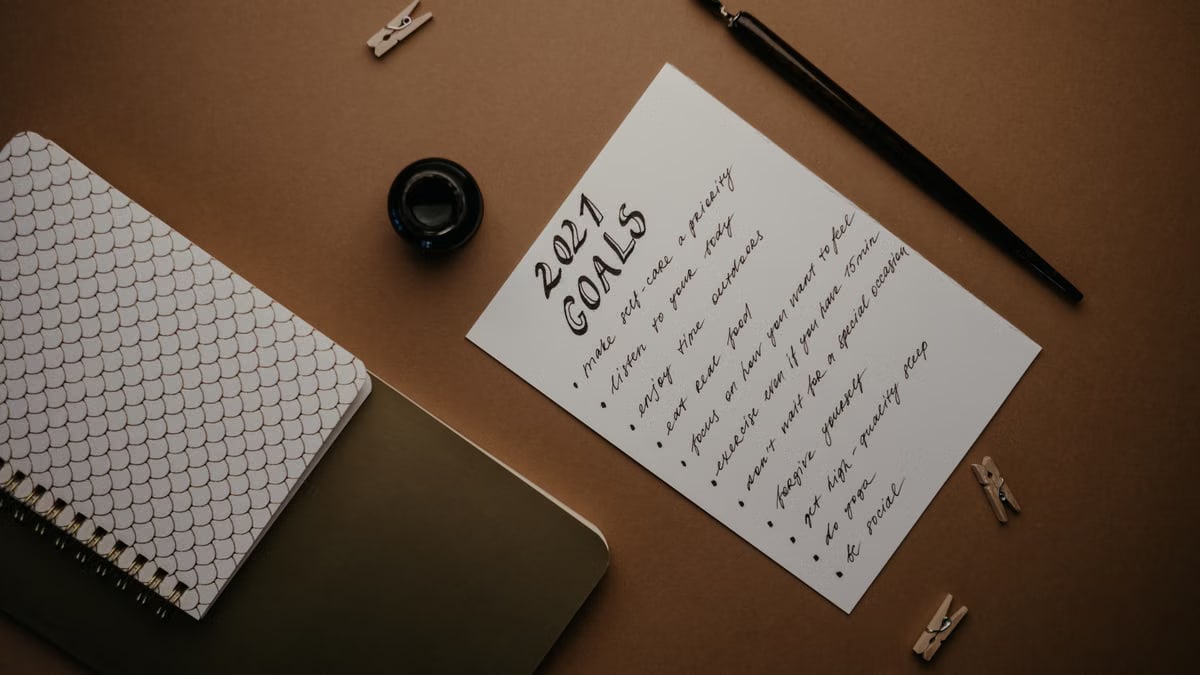 Stylish flat lay of a 2021 goals list with stationery on a brown background.